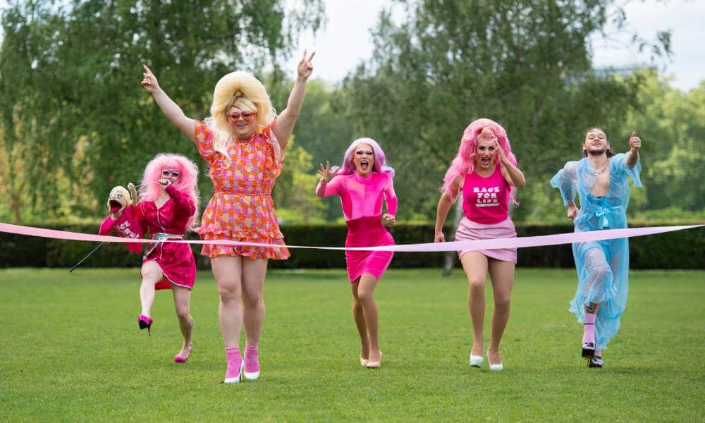 Drag artists including Ella Vaday, Kitty Scott-Claus, River Medway, Scarlett Fever and Boss are seen running towards a finish line while outside 