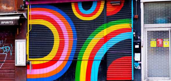 Dalston Superstore's exterior shutter, decorated in colourful rainbow display of colours. On either side are other small, lcoal London businesses.