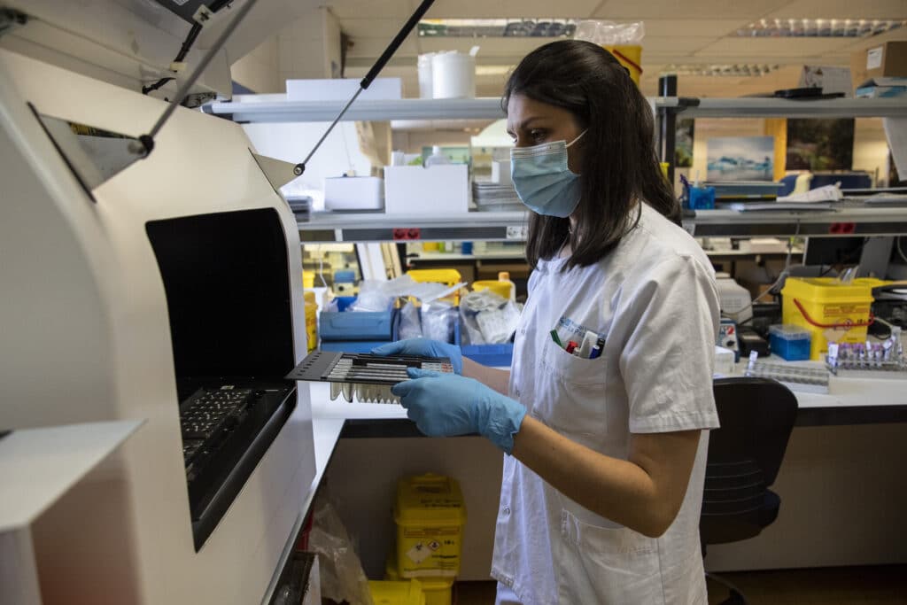 A medical laboratory technician places closes an automated nucleic acid extractor with suspected monkeypox samples inside