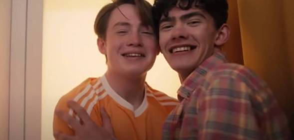 Actors Joe Locke and Kit Connor appear as their characters Charlie and Nick from the LGBTQ+ Netflix series Heartstopper. The characters are smiling while sitting close to each other in a photobooth