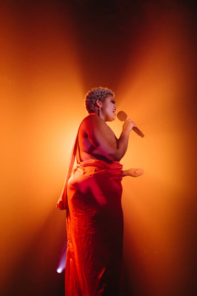 A performer singing with orange light behind them