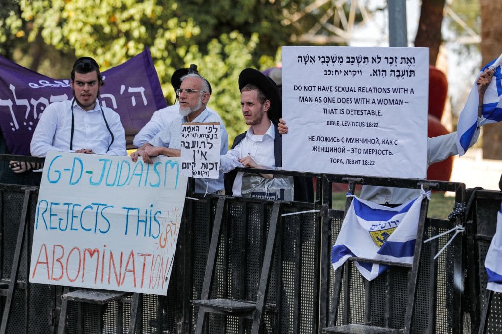Counter-protesters with drab white signs. One reads: God Judaism rejects this gay abomination