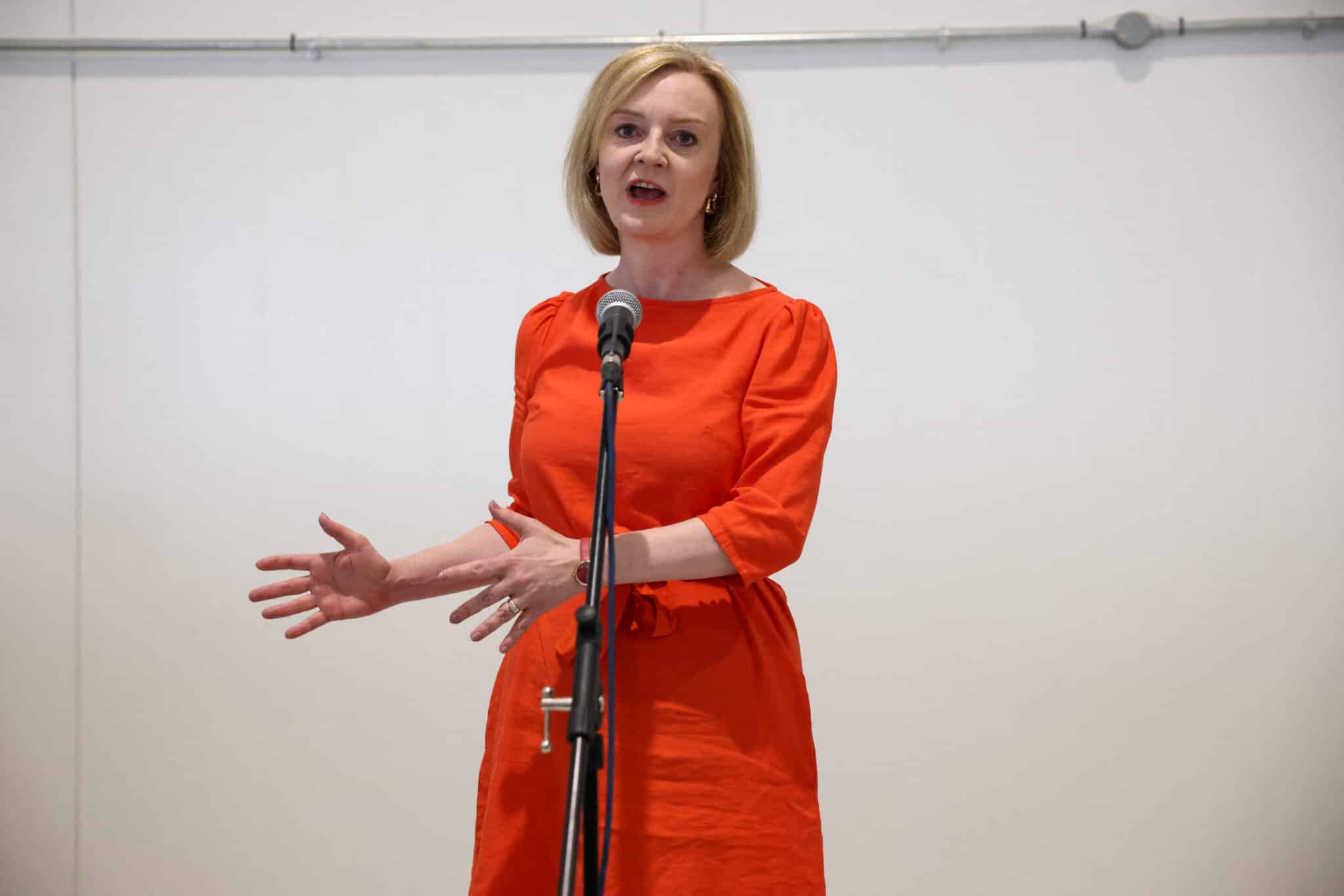 Liz Truss wearing an orange dress and speaking into a microphone.