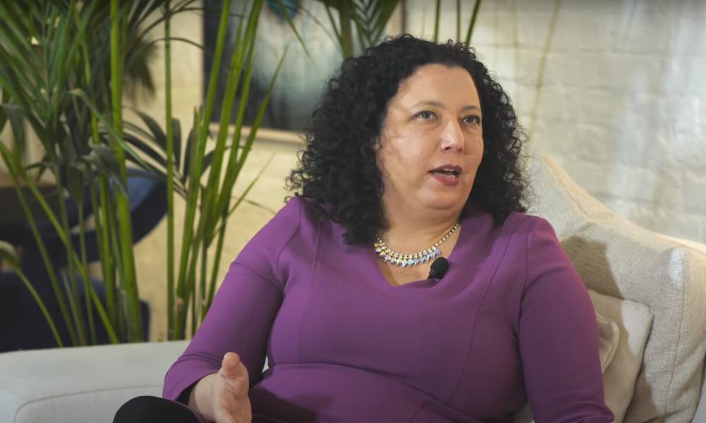 Maya Forstater wears a purple long sleeves top as she sits on a white couch during an interview