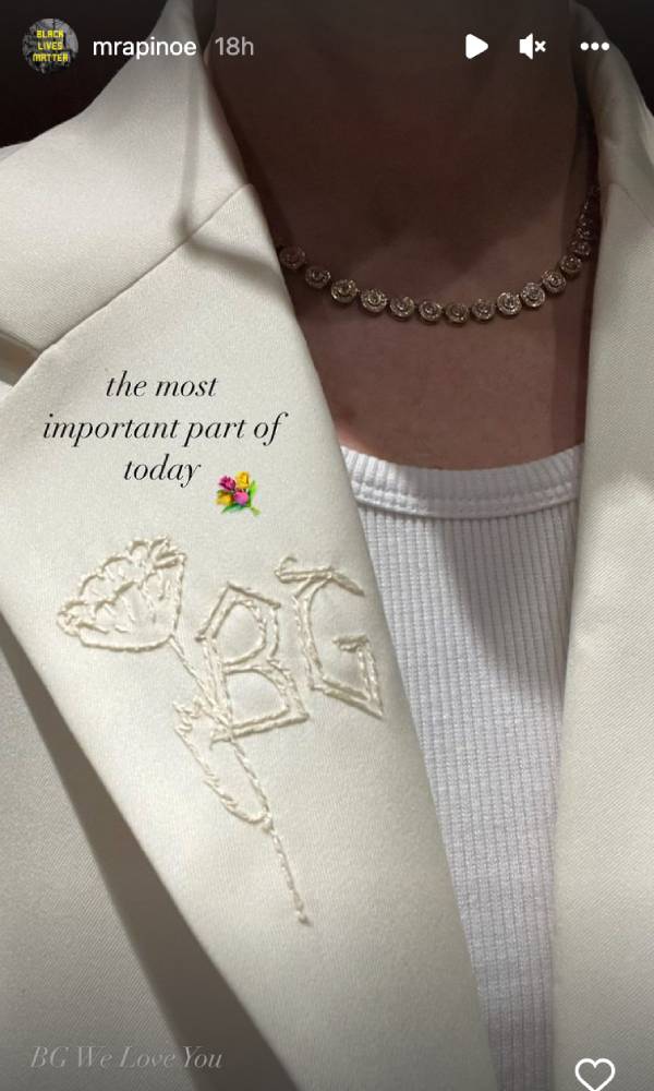Megan Rapinoe wears a white shirt and a cream blazer with Brittney Griner's initials (BG) embroidered on the label alongside a flower. Text on the image reads 'the most important part of today' and 'BG We Love You'