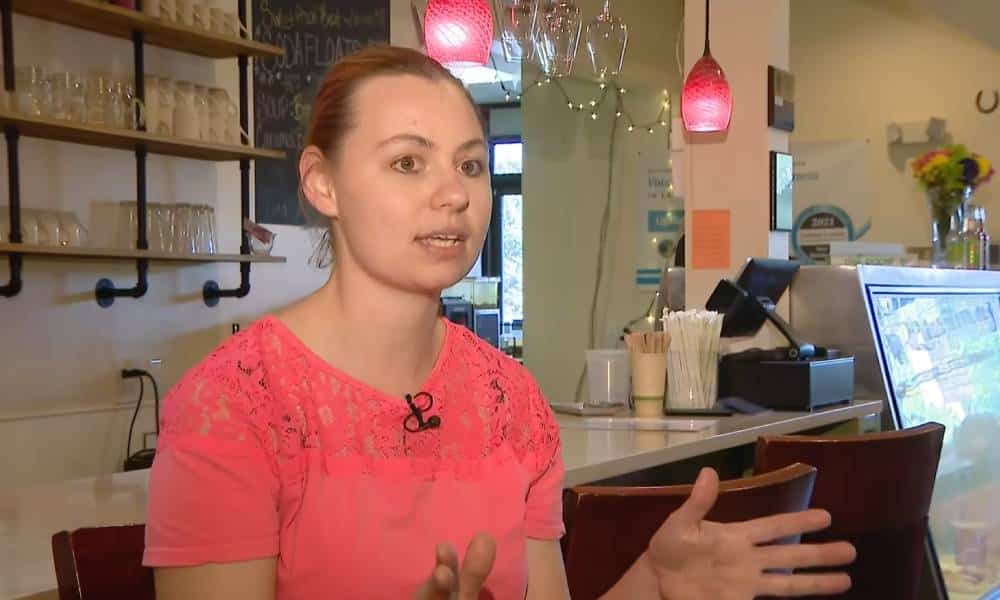 Corrina Sac wears a pink shirt as she sits in UpRising Bakery and Cafe during an interview about the bakery receiving threats over a planned family-friendly drag event
