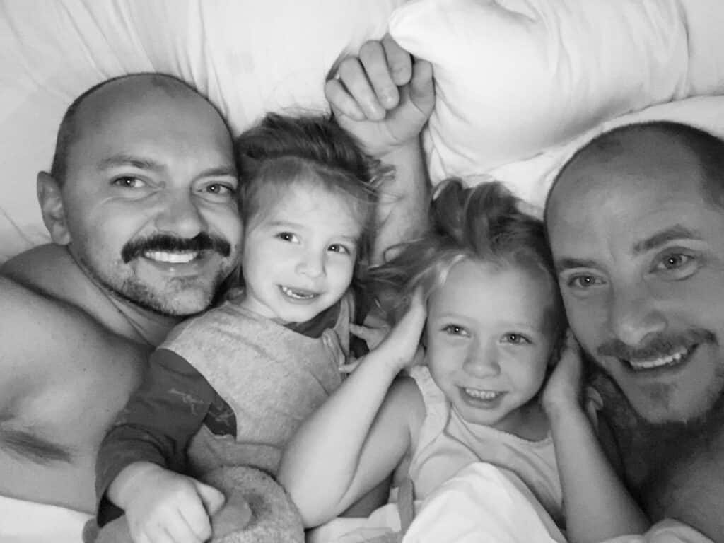 A black and white photo of Michael and Wes in bed, cuddling their two children