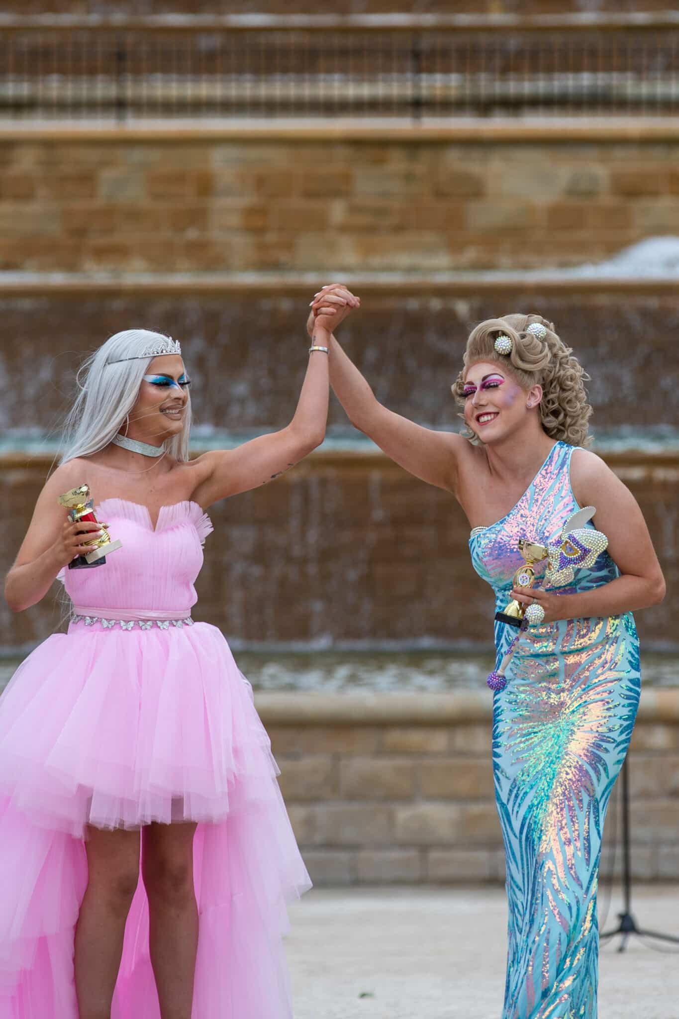 Drag queens hold hands in air with trophies 