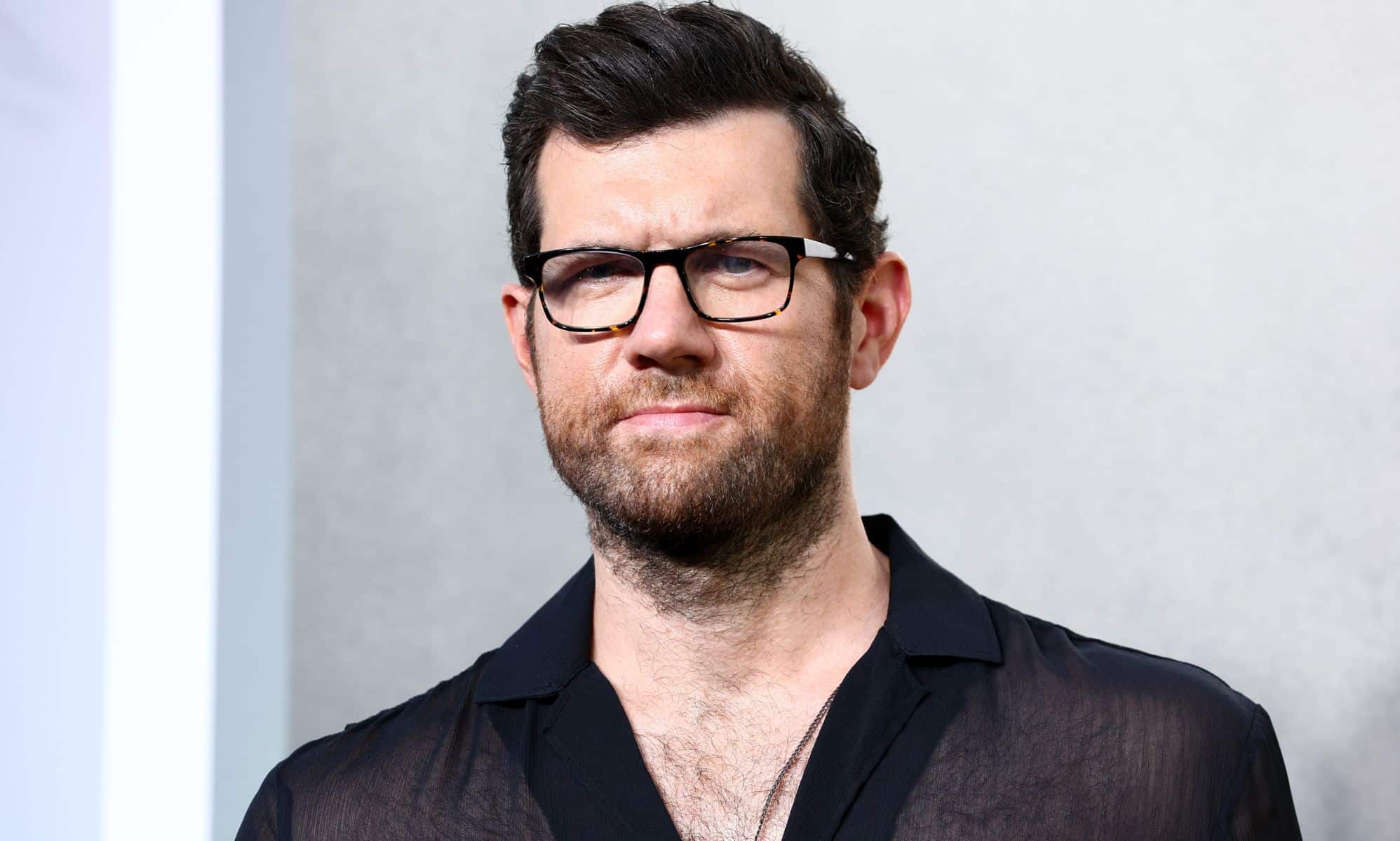 Billy Eichner wears a dark mesh top as he stares at the camera