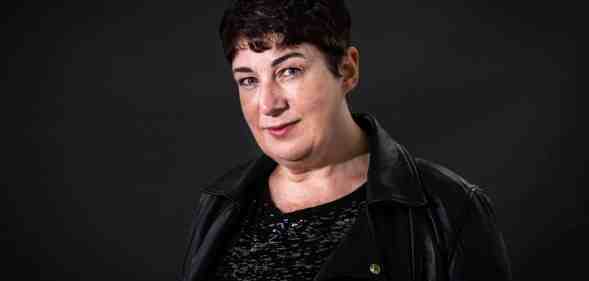 Joanne Harris wears a dark shirt and jacket while standing in front of a dark background