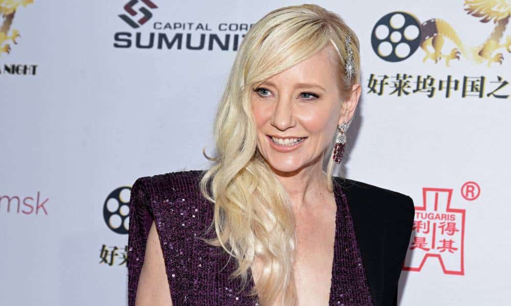 Anne Heche wears a purple sparkly outfit as she stares at someone off camera and smiles
