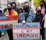 Several people join a protest outside the BBC. One person holds a sign that reads 'Transphobia is not unbiased' that is coloured with blue, pink and white stripes