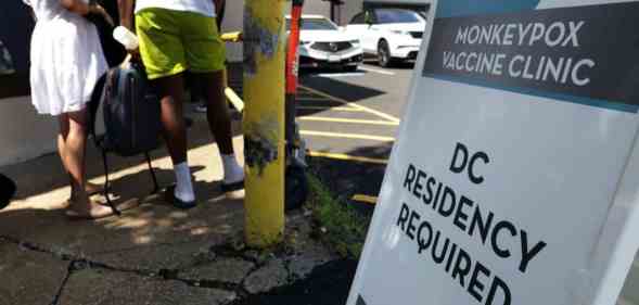 People wait in line for a monkeypox vaccine as a sign outside reads 'Monkeypox vaccine clinic DC residency required'