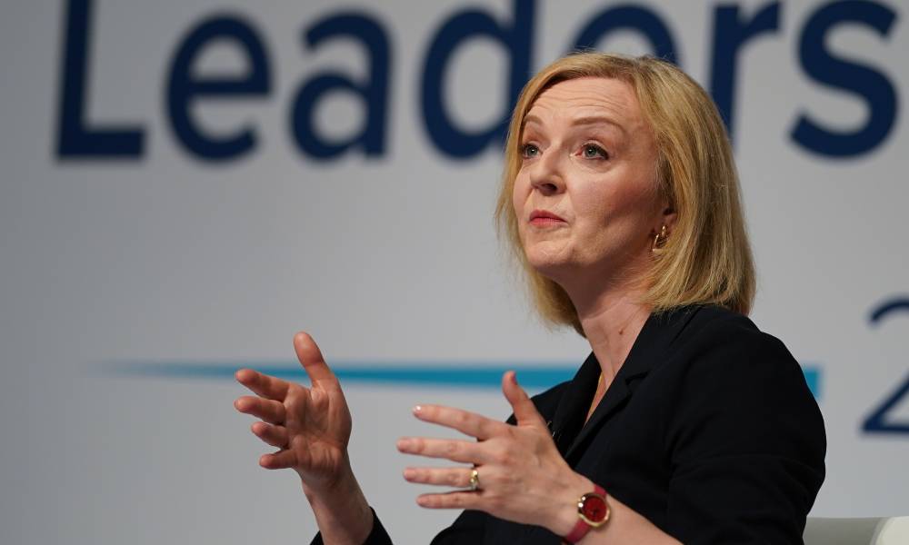 Liz Truss wears a dark outfit as she gestures with both hands in the air