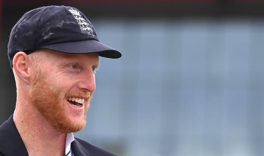 England captain Ben Stokes in blazer and cap smiles at the toss