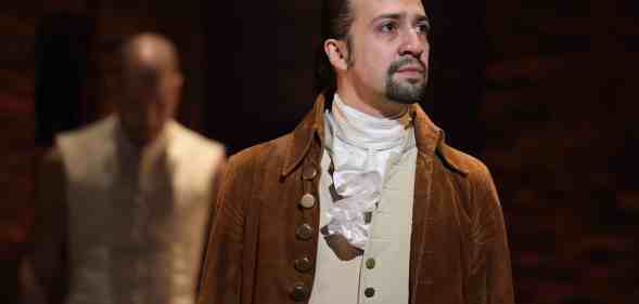 Lin Manuel Miranda, who plays Alexander Hamilton looks off into the distant wearing a brown jacket and cream waistcoat.