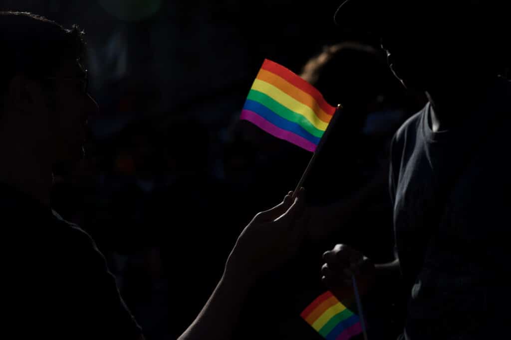 A small pride flag is waved in a dark street.