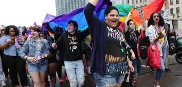 Participants, gathered in a crowd, hold up a rainbow LGBTQ+ flag during the Motor City Pride Parade at Detroit, Michigan