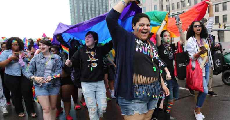 Participants, gathered in a crowd, hold up a rainbow LGBTQ+ flag during the Motor City Pride Parade at Detroit, Michigan