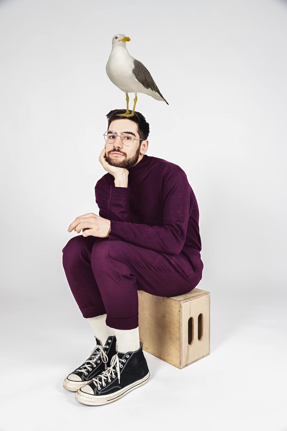 Sam Morrison sitting on a box with a bird perched on his head.