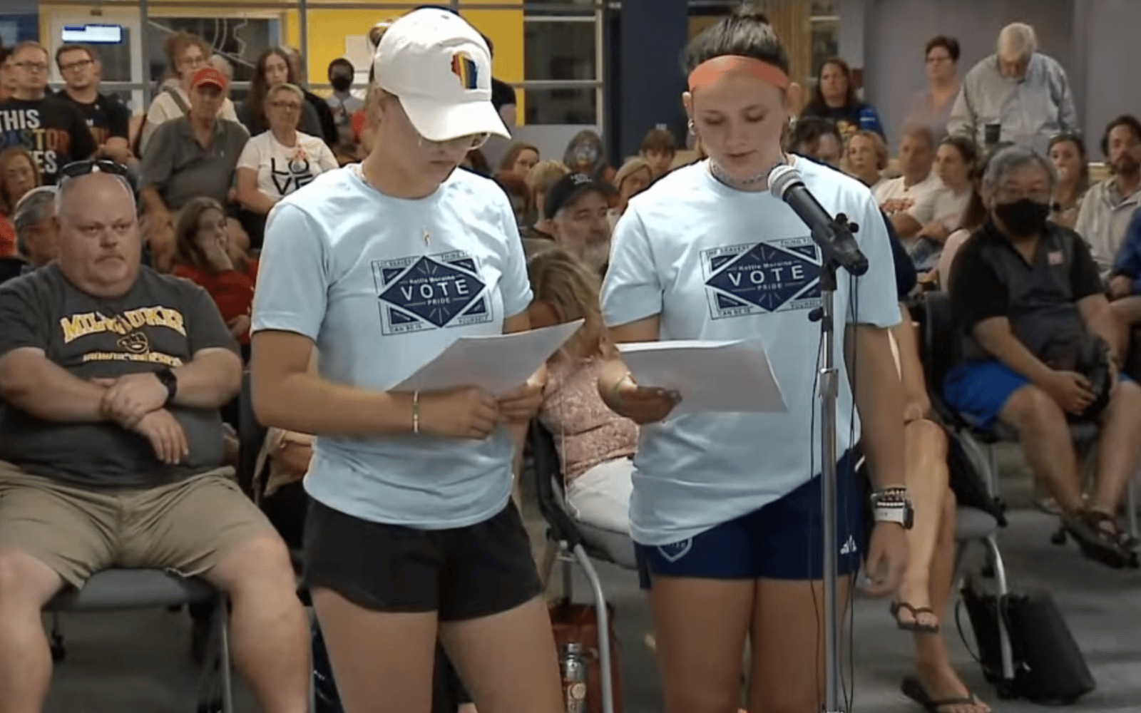 Two women stand in front of a packed crowd discussing notes they have written on paper.
