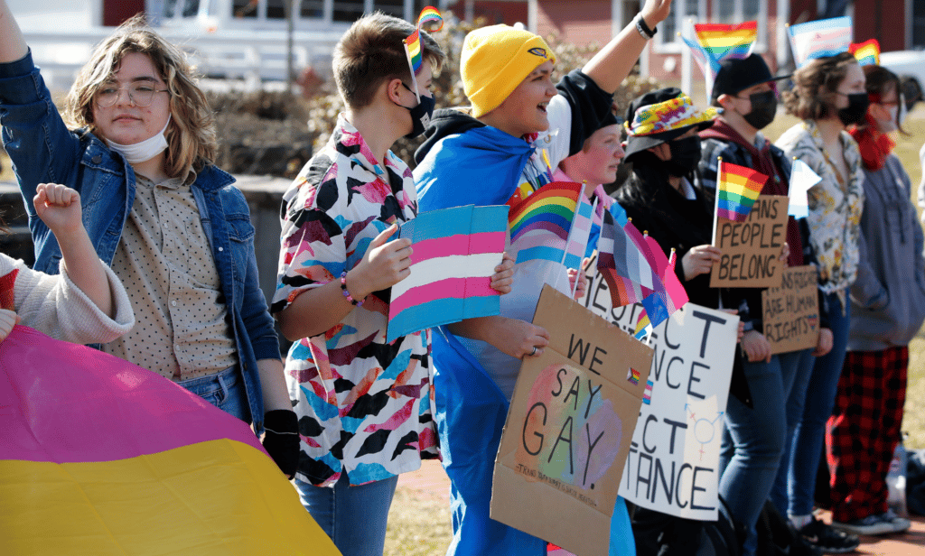 A group of students holding pro LGBTQ+ signs protest outside their school