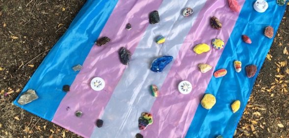 A flag laid out with stones at a vigil for the young trans man attacked during Pride celebrations