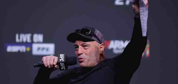 Joe Rogan raises a document in the air while speaking into a microphone excitedly.