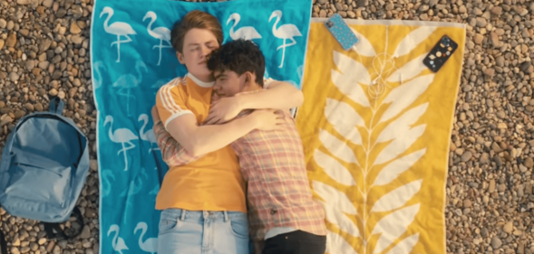 Heartstopper characters Nick and Charlie hold each other as they enjoy a day at the beach in an episode of the Netflix series