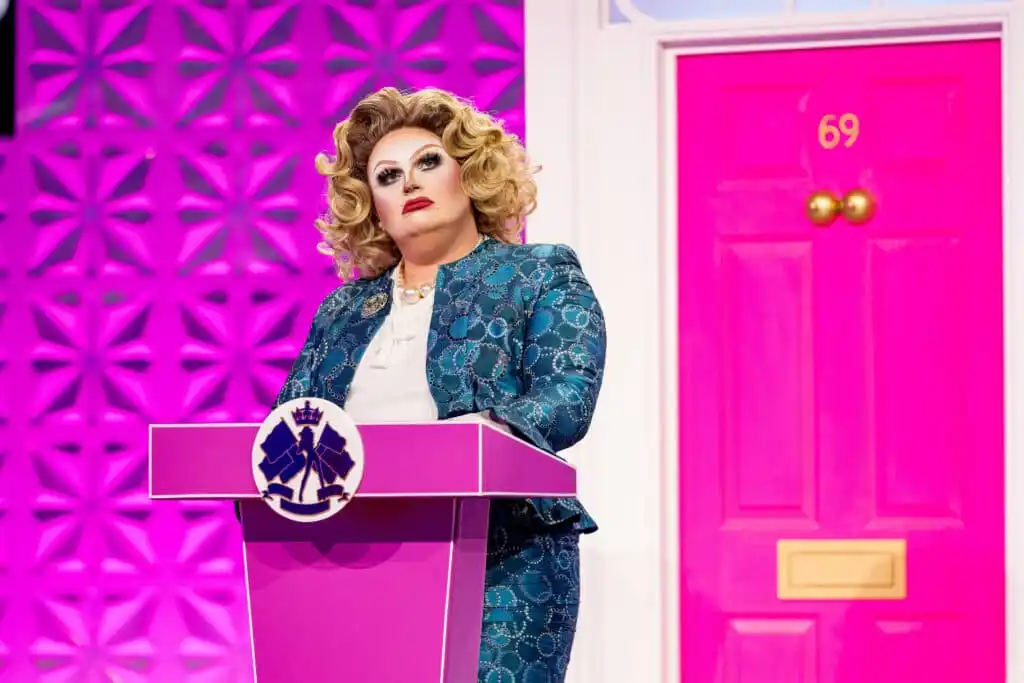 Drag Queen Pixie Polite standing behind a pink podium