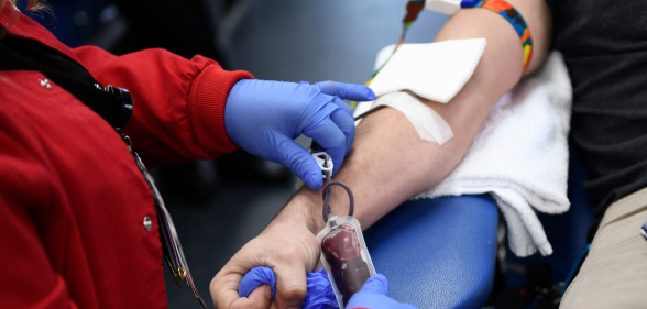 A picture of an individual's arm as they are donating blood, with a professional in blue latex gloves presiding over the operation.