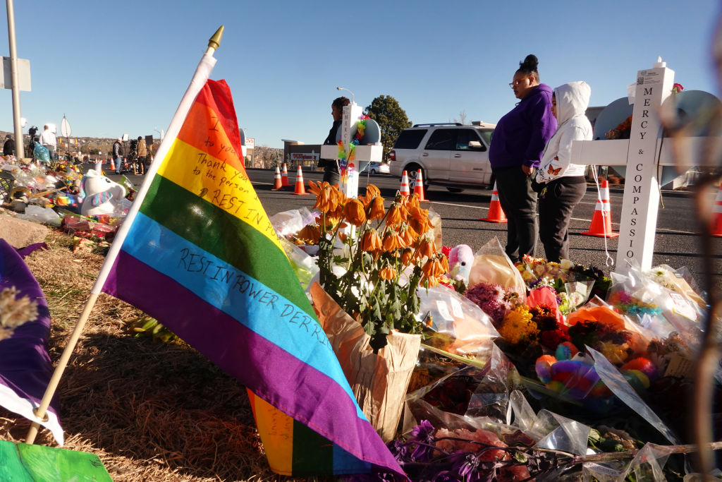 People visit a makeshift memorial near the Club Q nightclub on November 22, 2022 in Colorado Springs, Colorado. At the left hand side of the picture a Pride flag can be seen, and in the middle are flowers that have been left in memory of those killed at Club Q. 