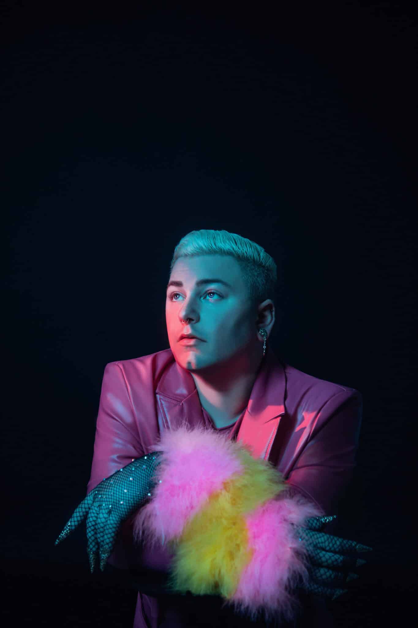 Pop artist Dead Method poses against a dark background wearing a pink suit. 
