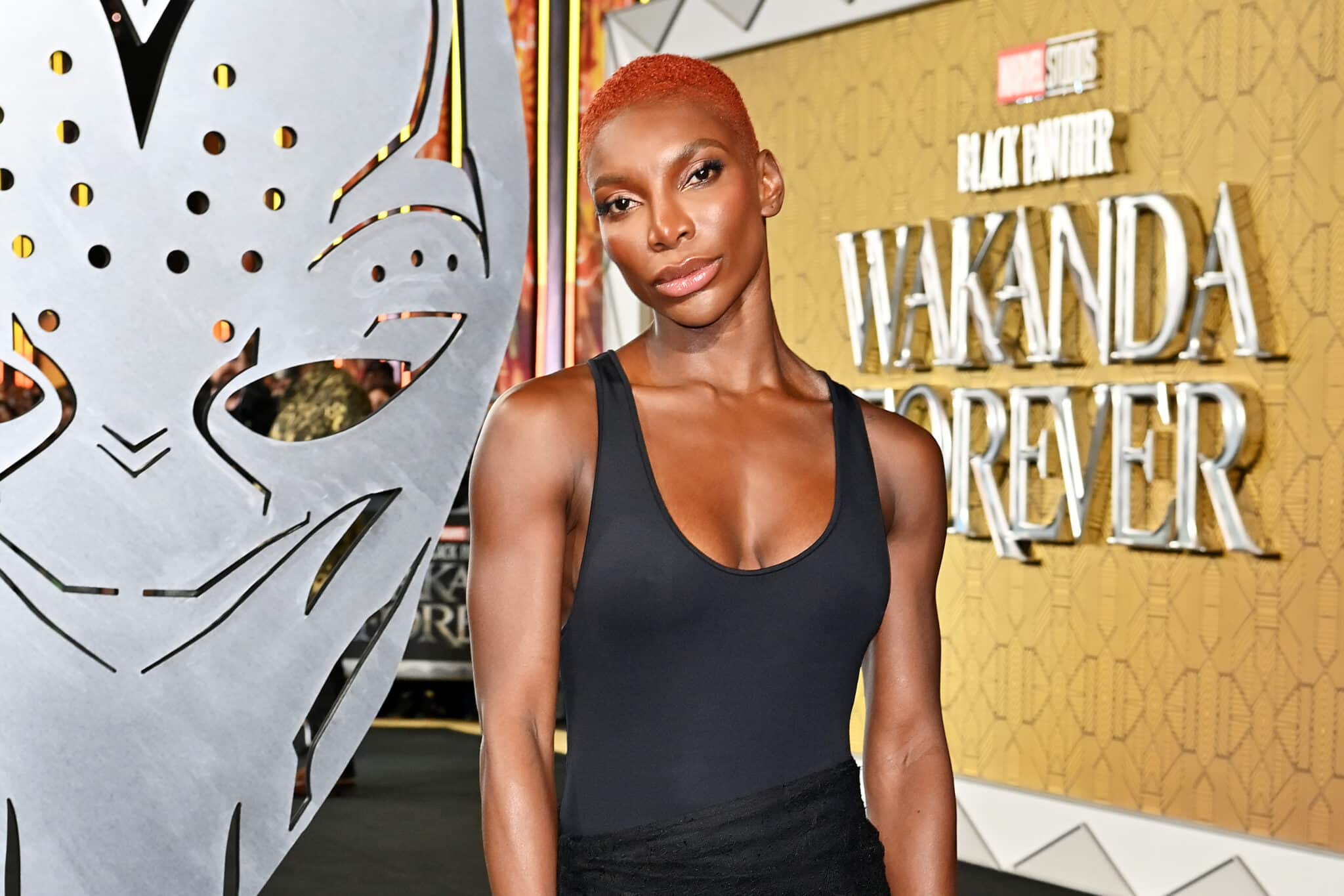 Michaela Coel posing bey an image of Black Panther's helmet during the Black Panther: Wakana Forever European Premiere. 