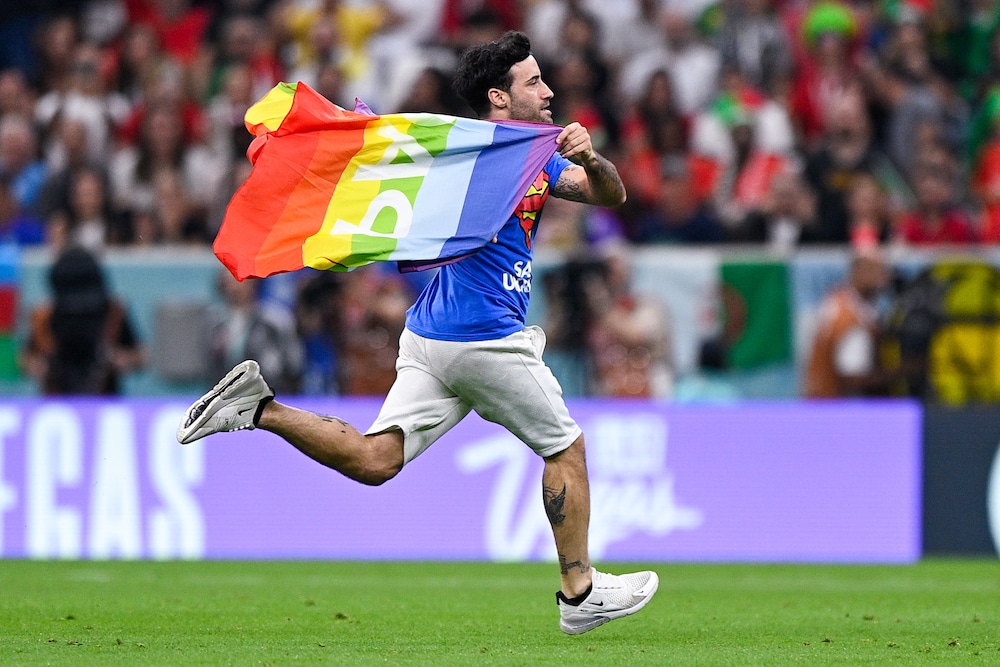The Qatar World Cup pitch invader runs across the pitch, holding a Pride flag like a cape