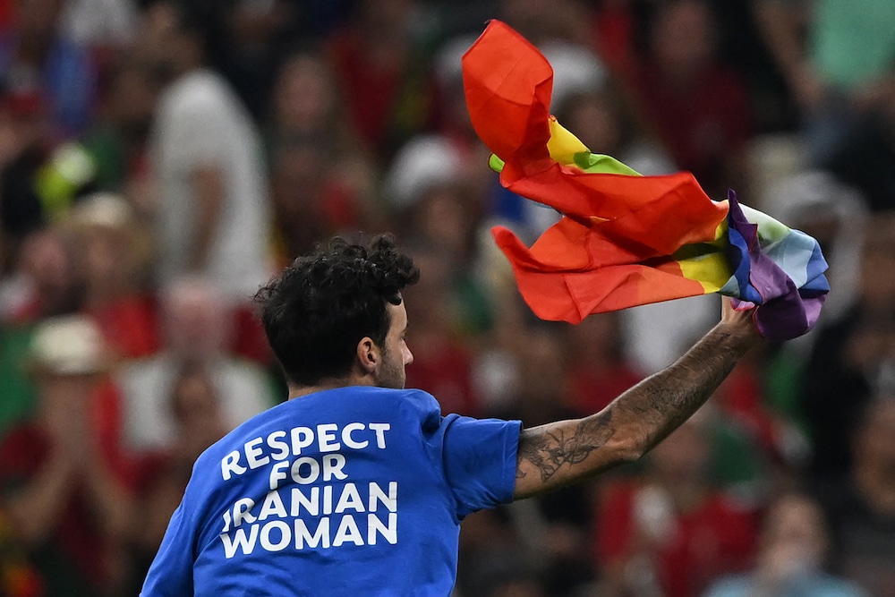 The Qatar World Cup pitch invader waves a pride flag in the air, he is shown from behind, his t-shirt reads "respect for Iranian women"