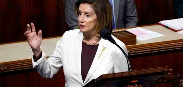 A photo of House Speaker Nancy Pelosi wearing a white suit jacket speaks behind a podium