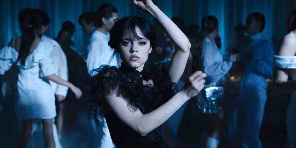 A still from Netflix's Wednesday series showing actor Jenna Ortega as Wednesday Addams dressed in a black dress and holding a dance pose