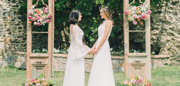 A same-sex couple gets married outside in white dresses