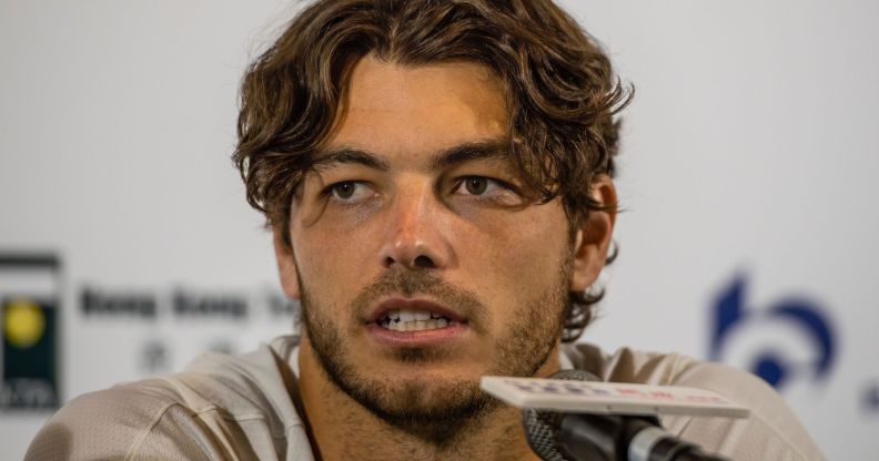 Taylor Fritz, wearing a white tee, speaks during a press conference into a small microphone.