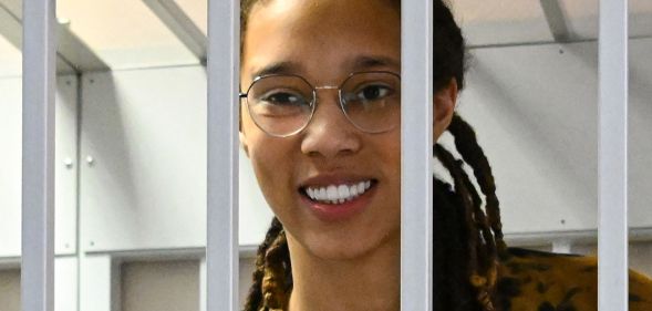 Brittney Griner smiles as she stands behind while bars while attending a Russian court hearing