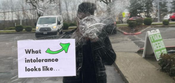 A photo showing the window of a bar in Seattle that had been shot. The glass is splintered and there is a sign stuck on the window just below the point of entry that says: "What intolerance looks like"