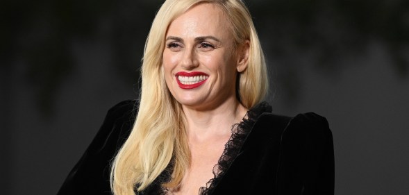 Photo of actor Rebel Wilson dressed in a black dress smiles for the cameras at a press event