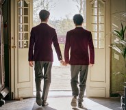 An image taken from Netflix's Instagram shows Young Royals actors Edvin Ryding and Omar Rudberg as Crown Prince Wilhelm and Simon dressed in their boarding school uniforms and walking hand in hand through some French patio doors with their backs to the camera