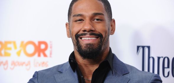 A photo showing professional wrestler Fred Rosser wearing a light blue suit jacket and black shirt smiling to the camera while on the red carpet.