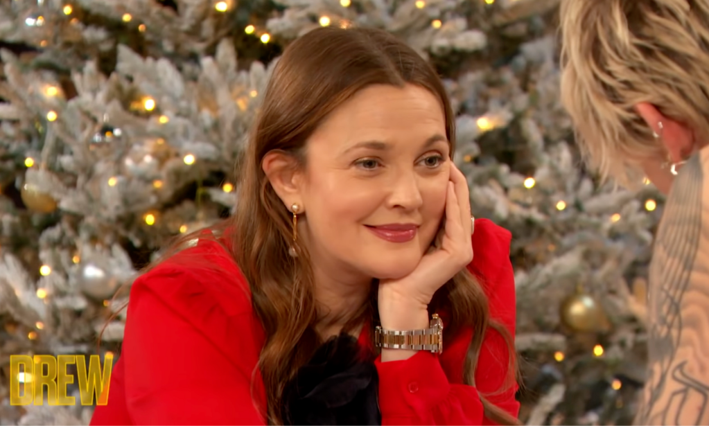 Drew Barrymore on The Drew Barrymore Show wearing a red jumped resting her chin on her hand