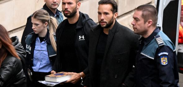 A photo shows controverisal influencer Andrew Tate and his brother Tristan Tate dressed in black arrive handcuffed and escorted by police at a courthouse in Bucharest