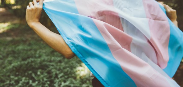 Close-up of a person walking while holding a transgender Pride flag behind their back