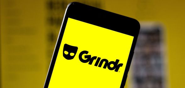 A phone showing a yellow depiction of the Grindr logo.