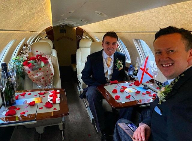 Paul and Alain on a plane on their wedding day. Both men are wearing tuxedos and the plane has been decorated.